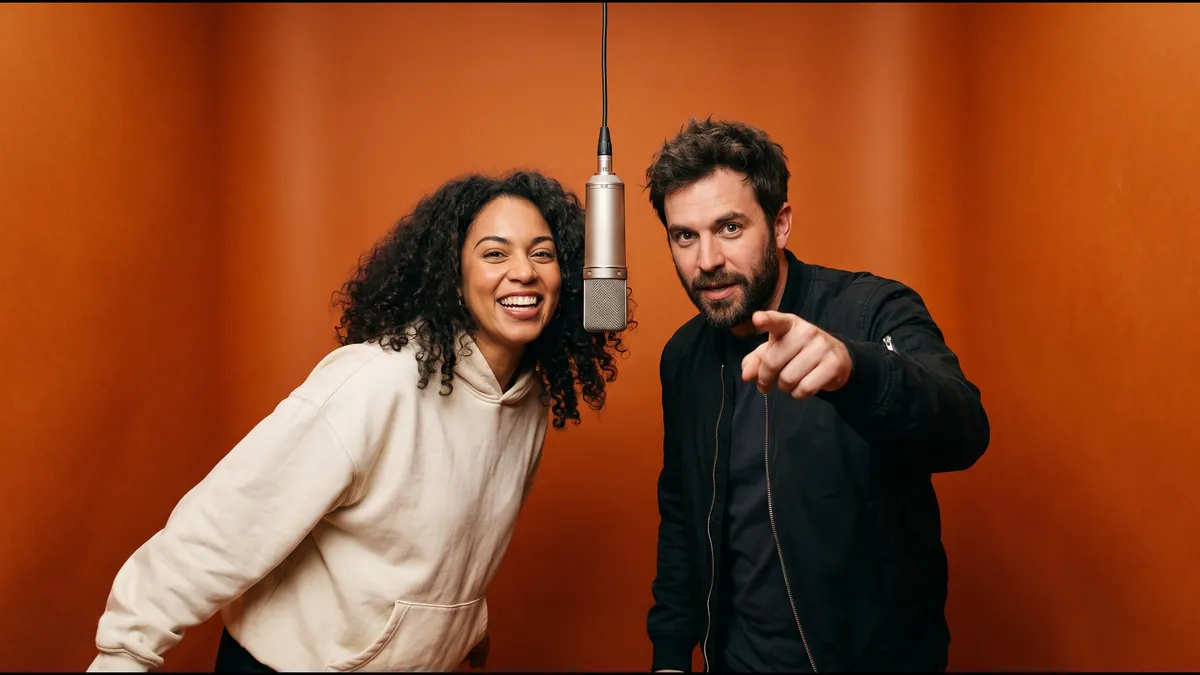 Two fictional adult friends in a seamless orange studio booth with a silver microphone hanging between them, the man pointing at the camera, an original AI image in the style of the hotel lobby trend